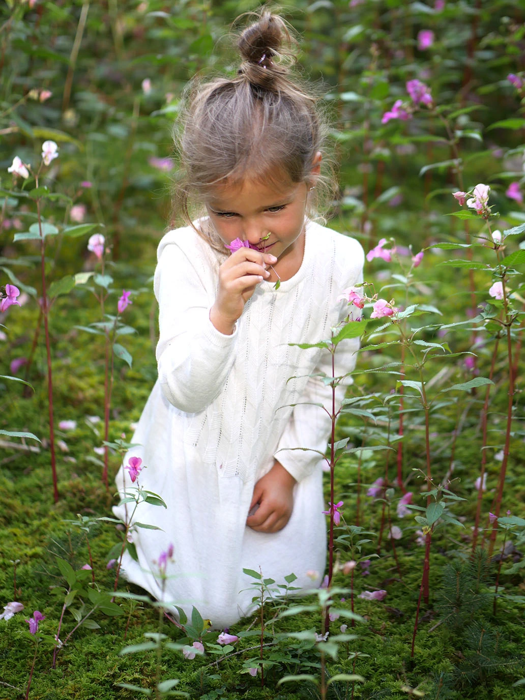 Ein junges Mädchen sitzt im Wald und riecht ein einder duftenden Blume.