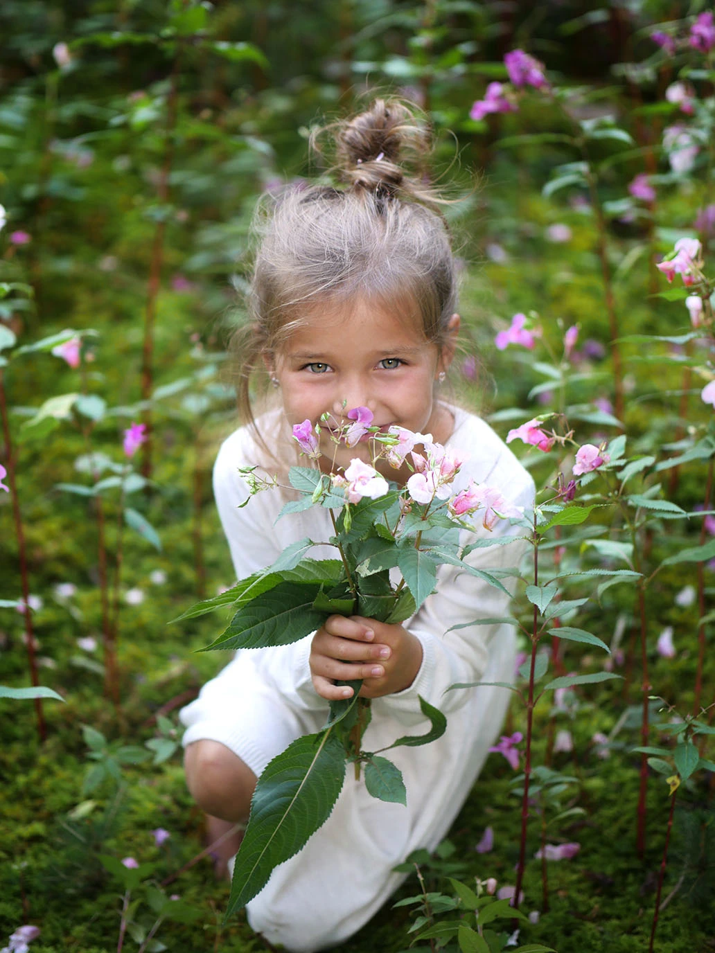 Ein junges Mädchen sitzt mit einem Blumenstrauß im Wald und blickt leuchtend in die Kamera.