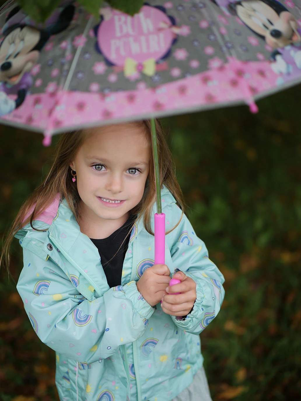 Ein junges Mädchen hält einen knall-bunten Regenschirm in der Hand. Sie blickt neugierig in die Kamera.