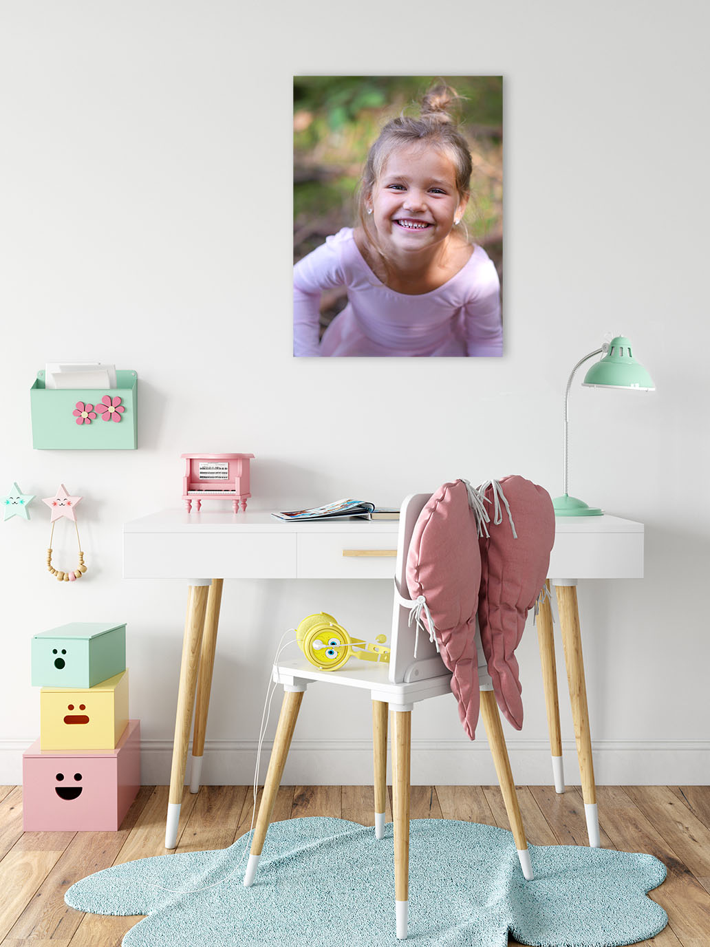 Ein helles Kinderzimmer. Über dem Tisch hängt ein wunderschönes, großes Wandbild von einem Mädchen, was strahlend in die Kamera lächelt